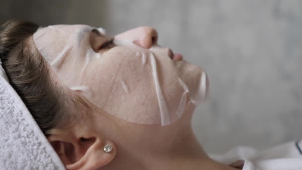 Profil kobiety w masce na tle szarej ściany. Nawilżacz skóry wykonany z naturalnych kosmetyków — Wideo stockowe