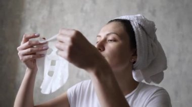 Yaşlanma ve yüz kırışıklıklarına karşı kozmetik doğal yüz maskesi. Yüzü nemlendirmek için havlu takan genç bir kadın maske takıyor.