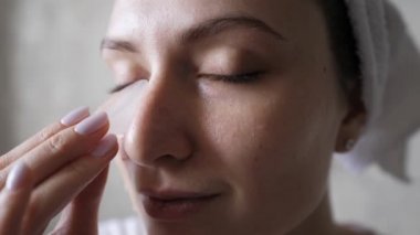 Donmuş suyla doğal yüz bakımı. Yaşlanma ve kırışıklıklara karşı cilt için buz kullanımı. Kafasında havlu olan beyaz bir kadın kameraya bakar ve cildini nemlendirir.