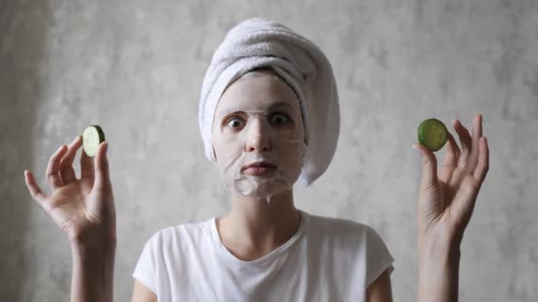 A woman in a face mask is having fun with round cucumbers, looking at the camera and fooling around. Natural Regenerating Skin Care — Stock Video