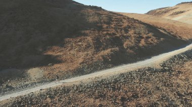 Hava. Bir hipster adam dondurulmuş lav ve volkanik kum ile, bir volkanın dibinde bir yol boyunca bir sırt çantası ile yürüyor. Tenerife, Teide Ulusal Parkı.