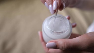 Kozmetik ürünü, beyaz kavanoz. Elinde kürek olan bir kadın eli, yüz derisi için nemlendirici çıkarır. Sağlık, temizlik, sabah makyajı.