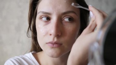 Kadın güzelliği ve refahı. Sıhhatli cilt bakımı yakın plan. Bir kız küçük bir aynaya bakar ve yüzüne bir fırçayla şeffaf bir krem sürer.