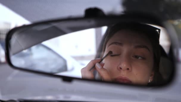 美しい白人の少女は車の後部ビューミラーを見て、彼女の目に影を置きます.車の中で法律の違反。輸送中の女性が集まる — ストック動画