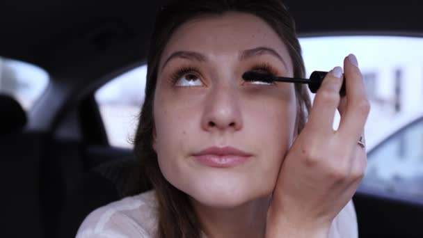 Die Frau im Auto schminkt sich. Schönes Frauenporträt in Nahaufnahme, während Wimpern mit Wimperntusche überzogen werden — Stockvideo