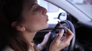 Arabanın direksiyonunu elinde tutan beyaz bir kıza dudak parlatıcısı sürüyorum. Tehlikeli sürüş. Direksiyonda makyaj var.