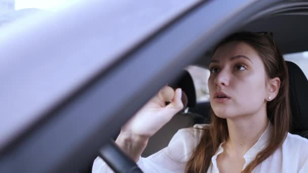 Una mujer atractiva pone un rubor con un cepillo grande mientras está sentada detrás del volante de un coche. Temprano en la mañana, una mujer de negocios llega tarde al trabajo. Tonificación en polvo para la cara — Vídeo de stock