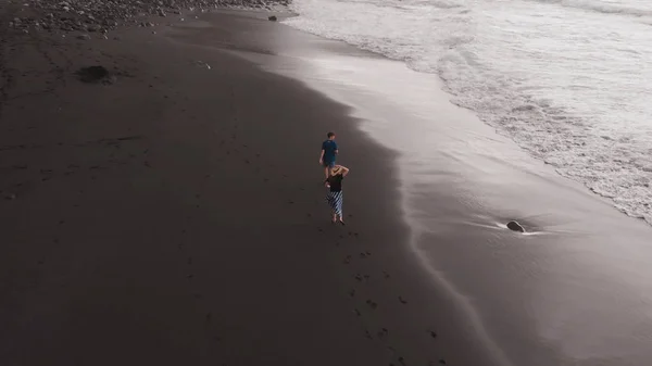 Вид с воздуха на черный пляж. Мужчина и женщина быстро бегут по вулканическому песку вдоль Атлантического океана, на Тенерифе. Испания — стоковое фото