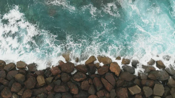 Top down view. The construction of stones to strengthen and protect the coast from the ocean - a birds-eye view. Large stones and the ocean of turquoise color. — Stock Photo, Image