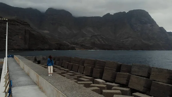 Statische weergave van de drone op een jong meisje staande op een Pier op een donkere dag. Agaete, Gran Canaria, Spanje — Stockfoto