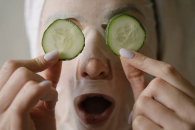 Eğlence, yüz bakımı, kaldırma ve su alma. Genç ve güzel bir kadının gözlerinden yuvarlak salatalıklar düşer.