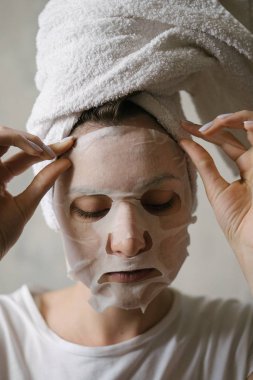 Genç bir kadın yüzünden nemlendirici bir maske çıkarıyor. Güzellik, cilt bakımı, estetik ameliyat