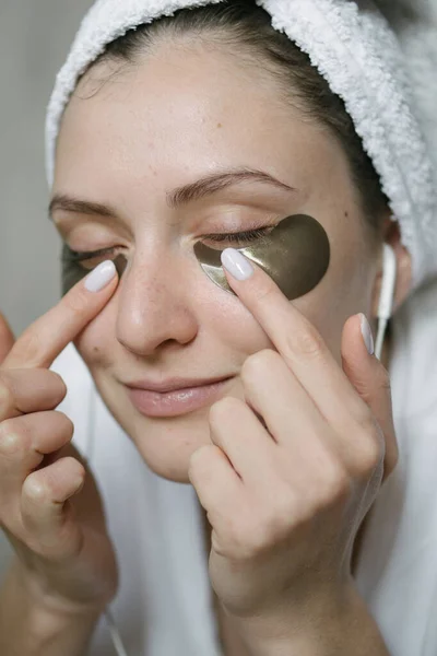 Natural skin care with bio cosmetics. Morning makeup, removing bruises under the eyes with the help of patches. Skin lifting around female eyes while listening to music