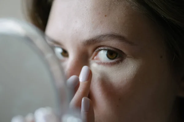 Cosméticos e cuidados da pele. Uma bela mulher olha para a câmera e aplica uma base de tonificação sob seus olhos — Fotografia de Stock