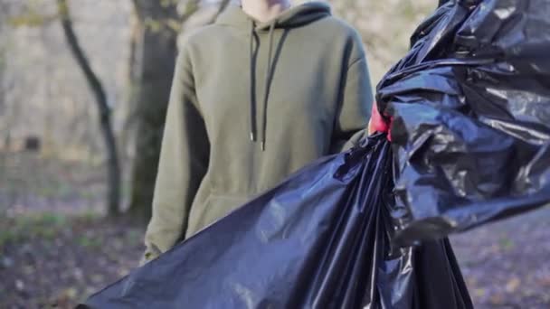 Una voluntaria muestra como y una bolsa de basura negra, después de limpiar el bosque de plástico. Aspectos medioambientales — Vídeo de stock