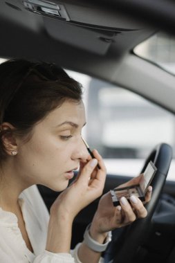 Makyaj arabada. Beyaz bluzlu çekici bir kadının portresi. Göz farı sürdüğü için fırçaya üflüyor.