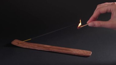 A womans hand sets fire to an aromatic stick in a stand on a black background. Spiritual smoke, strong smell for the ceremony. Natural aromatherapy. Black background, static shot.