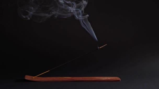 Ароматическая палка курит в стойке на черном фоне. Ладан для расслабления и медитации, азиатский предмет. Буддизм, естественный поток и магия — стоковое видео