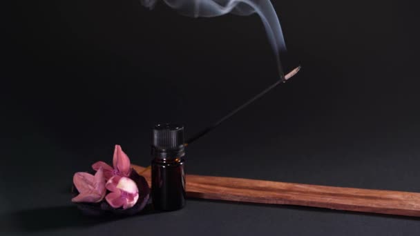 Aromatic objects are isolated on a black background. Incense, aromatic oil and dry flowers. Smoke goes up from a stick in a wooden stand — Stock video