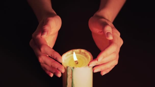 Frauenhände über der brennenden Kerze in Großaufnahme. Magisches Feuer, prophezeit die Hexe. Isoliert auf schwarzem Hintergrund, eine statische Aufnahme — Stockvideo