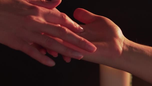 Womens hands predict on the mans palm, isolated on a black background next to a burning candle. The concept of palmistry, magic and clairvoyance. A woman reads lines on males hand — Wideo stockowe