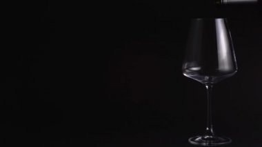The sommelier pours red wine into a beautiful empty glass. Tasting wine in a bar or restaurant. Isolated, black background