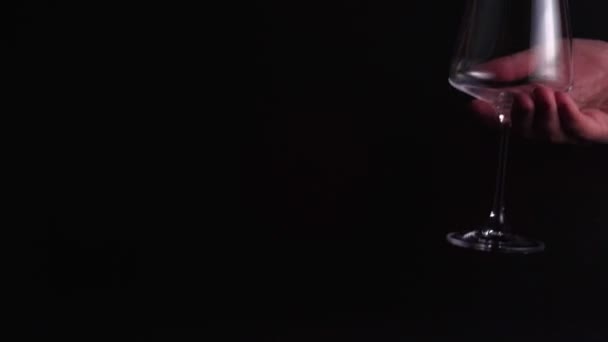 A mão do homem coloca um copo vazio para o vinho sobre um fundo preto e depila-o. Tiro estático isolado. Servindo um jantar de luxo, o conceito de vinificação e degustação de álcool — Vídeo de Stock