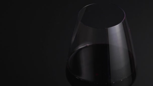 O vinho tinto flui para um frágil copo sobre um fundo preto. Sommelier enche um copo de bebida alcoólica doce em um bar close-up, isolado — Vídeo de Stock