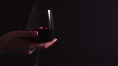 Alcoholic drink in a transparent glass - a woman sommelier rotates a glass with wine on a black background. The process of testing the smell and checking red wine