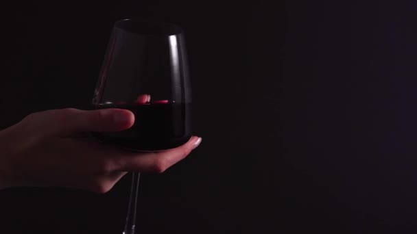 Bevanda alcolica in un bicchiere trasparente - un sommelier donna ruota un bicchiere con vino su sfondo nero. Il processo di verifica dell'odore e il controllo del vino rosso — Video Stock