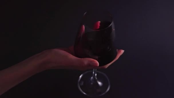 The smell of wine - a womans hand rotates a glass on a black background. A professional in a bar or restaurant tastes an alcoholic beverage — Stockvideo