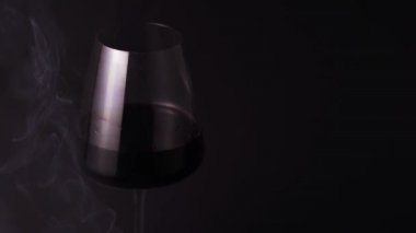 Alcohol and smoke is isolated against a black background, close-up. Red wine in a special beautiful glass