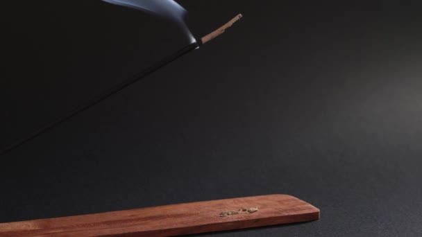 Eastern aromatic smoke. Incense stick burns in a wooden stand on a black background. Natural smoke moves up — Stock Video