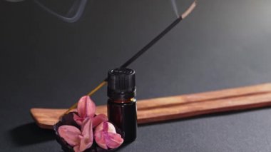 Aromatic oil in a black small jar, flowers and steaming incense. A static shot against a black background. The smell of the east, the concept of massage and meditation