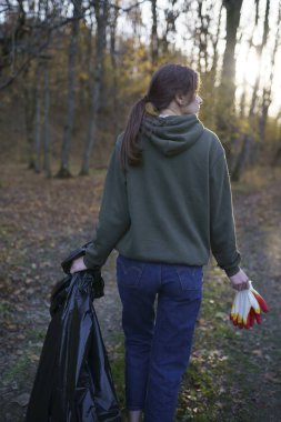 Sonbahar manzarasında plastik bir torbayla güneşte güzel bir gönüllü kız. Açık havada çöp ve plastik koleksiyonu