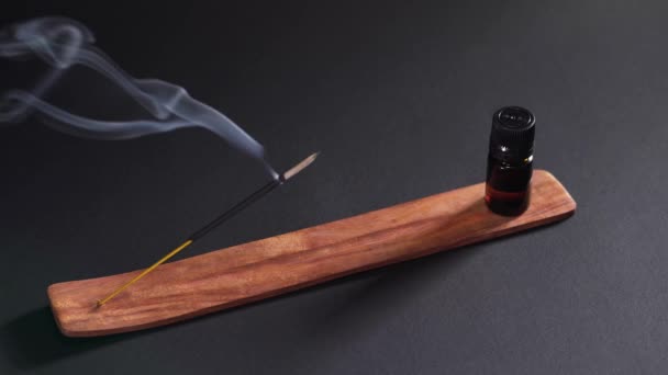 Aceite aromático e incienso humeante sobre un soporte de madera sobre un fondo oscuro. Artículos para aromaterapia, meditación y masaje — Vídeo de stock