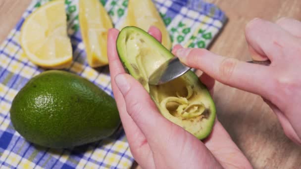 The womans hand takes out a spoonful of flesh from half of the avocado to make guacamole. Recipe for Mexican dishes, close-up. Delicious, healthy and natural food — стокове відео