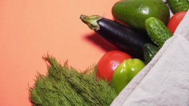 Cotton bag with vegetables on a coral background, zooming shot. Using recycled materials instead of plastic. Beautiful vegetables, healthy lifestyle