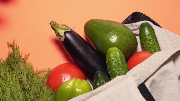 La mano del hombre saca un aguacate fresco de una bolsa de algodón sobre un fondo de melocotón. Bolsa ecológica, concepto de protección del medio ambiente. Comida plana — Vídeo de stock