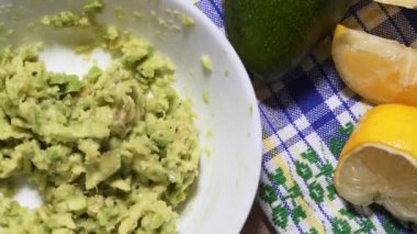 Dilimlenmiş avokadoyu yakın plan beyaz bir kasede karıştırıyorum. Masa örtüsü ve limonun arka planına karşı sağlıklı vejetaryen atıştırmalığı.