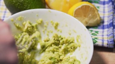 Masada geleneksel guacamole sosu pişiriyorum, yakın plan. Beyaz bir kâsede yeşil çiğ avokado, güzel bir masa örtüsüne karşı.