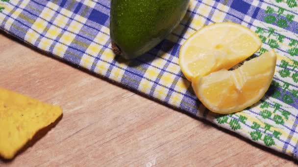 Gezouten maïs chips nachos gegoten op een houten tafel, tegen de achtergrond van citroen en avocado. Lekkere en schadelijke snack, fastfood — Stockvideo