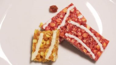 Different pieces of granola bars are taken from a white plate stop motion