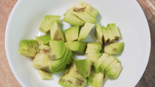 Добавление нарезанных ломтиков сырого авокадо в белую миску крупным планом, остановка движения — стоковое видео