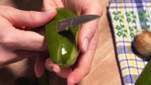 Cleansing the avocado from the peel with a silver knife, static close-up shot. Cooking guacamole in the kitchen, a woman holds a ripe avocado — Stok video