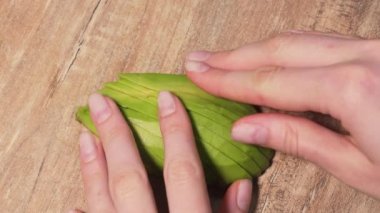 Womens hands lay out pieces of sliced avocado on a wooden table. Ingredient for salad or guacamole. Healthy food concept