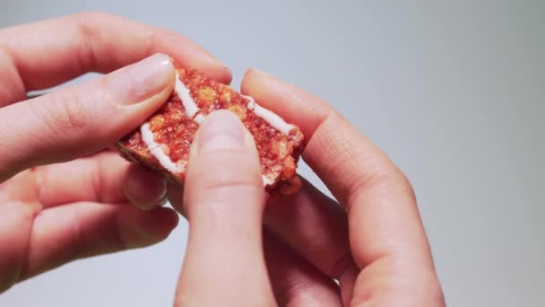 Las manos de las mujeres rompen una barra de proteína roja con el sabor de las fresas y frambuesas. Dieta saludable vegetariana para meriendas, cereales y gelatina — Vídeos de Stock