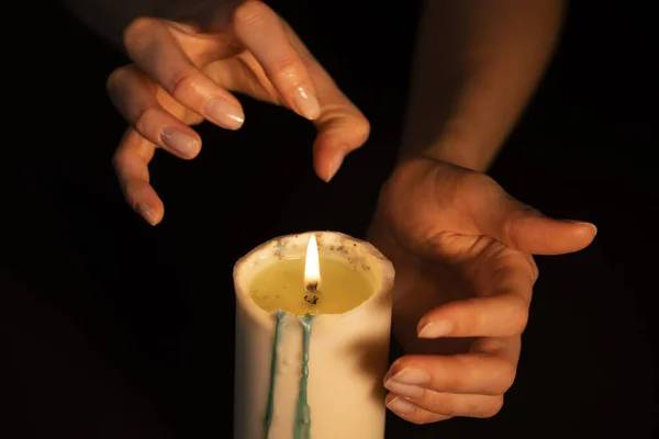 Eller siyah arka plandaki bir mumun üzerinde hokkabazlık yapıyor, yakın plan. Ruhani seans, geleceği gören falcı.