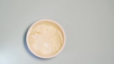 The person gradually eats yogurt in a paper glass. Natural yogurt disappears in a glass on a white background, top view, isolated, stop motion