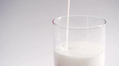 A person pours fresh organic yogurt into a transparent glass. Milk yogurt slowly fills the glass, isolated on a white background